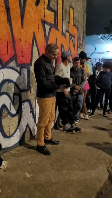 Voluntário do instituto conversando com pessoas em fila, à noite